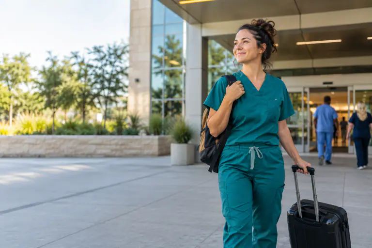 Travel nurse with a rolling suitcase and scrubs outside a hospital entrance